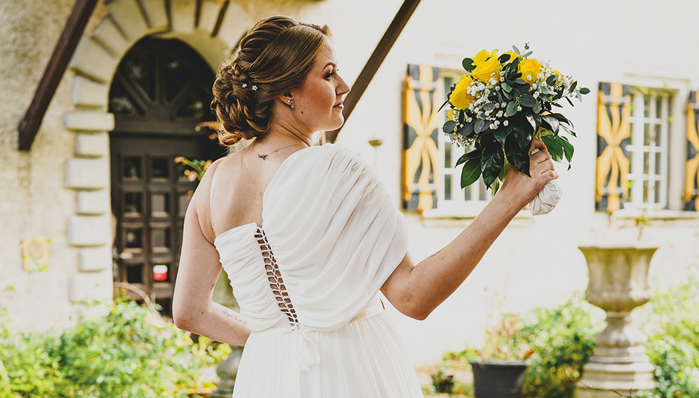 Braut mit Blumenstrauß vor historischem Gebäude.